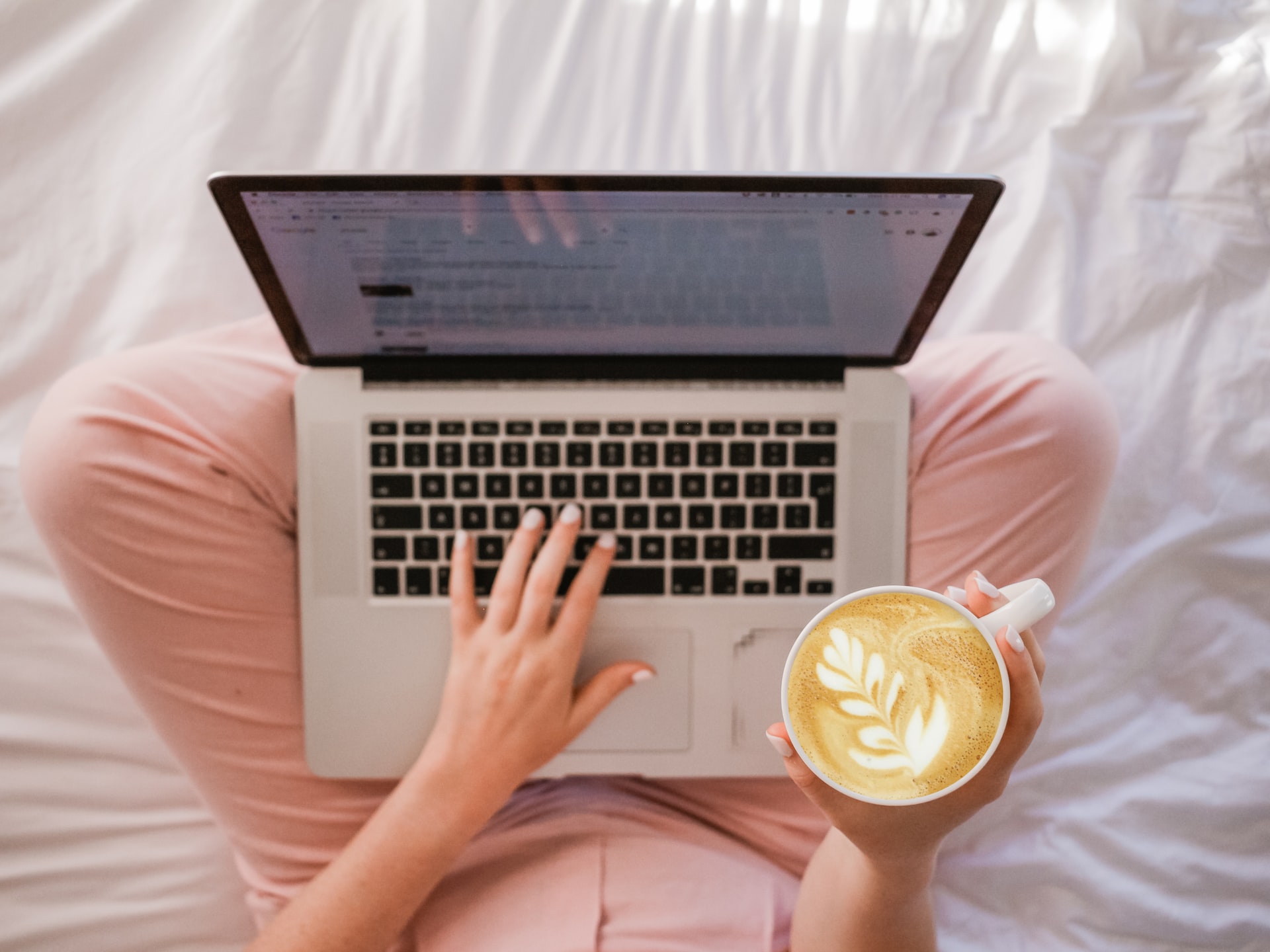 women sitting on the floor with a laptop in her lap and a coffee mug in her hand.